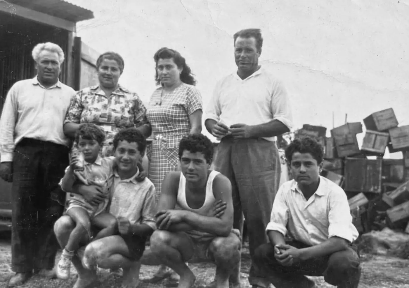 Rupert's family in the 1950s: four adults standing and four boys crouched in front, the men in open-collar shirts, trousers and a singlet